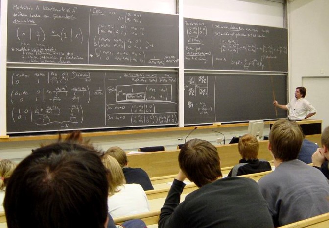 Professor demonstrates equations at blackboard.