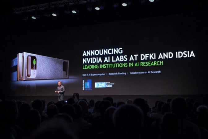 NVIDIA DGX-1 AI スーパーコンピューターの早期導入のプレゼンテーションを背に講演する NVIDIA の共同創立者兼 CEOジェンスン・フアンの画像