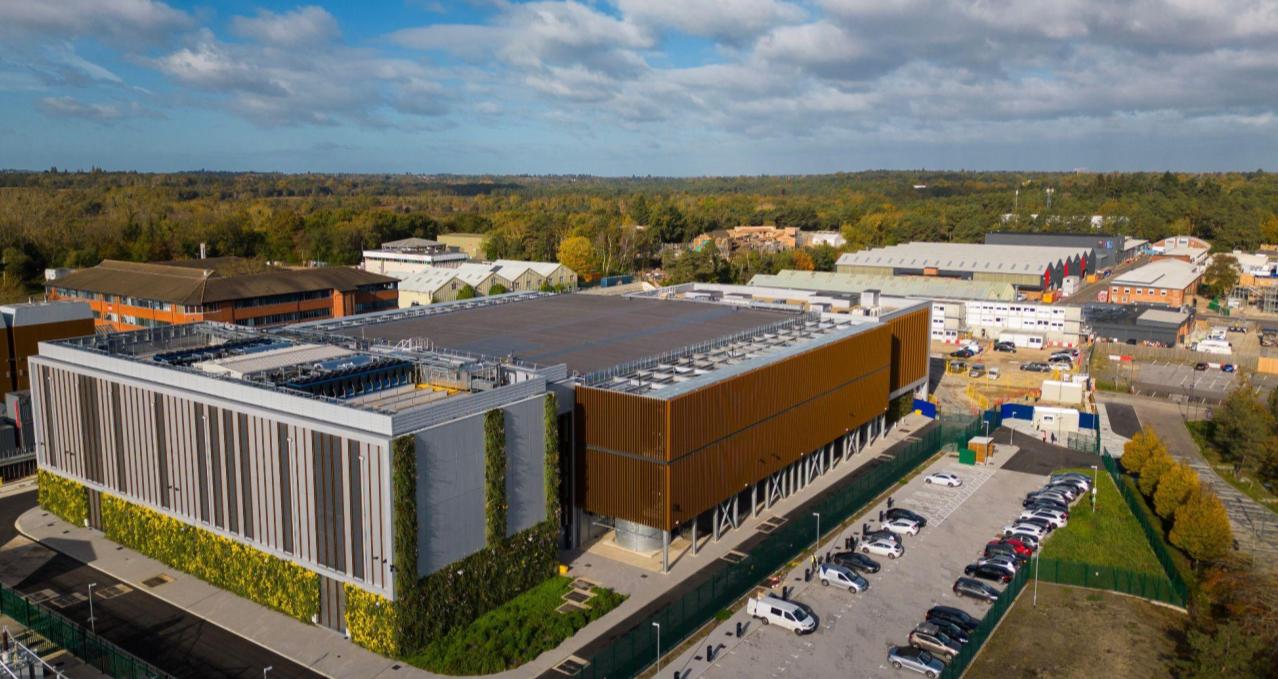 Image of Nebius AI factory in the UK surrounded by a parking lot and green foliage.